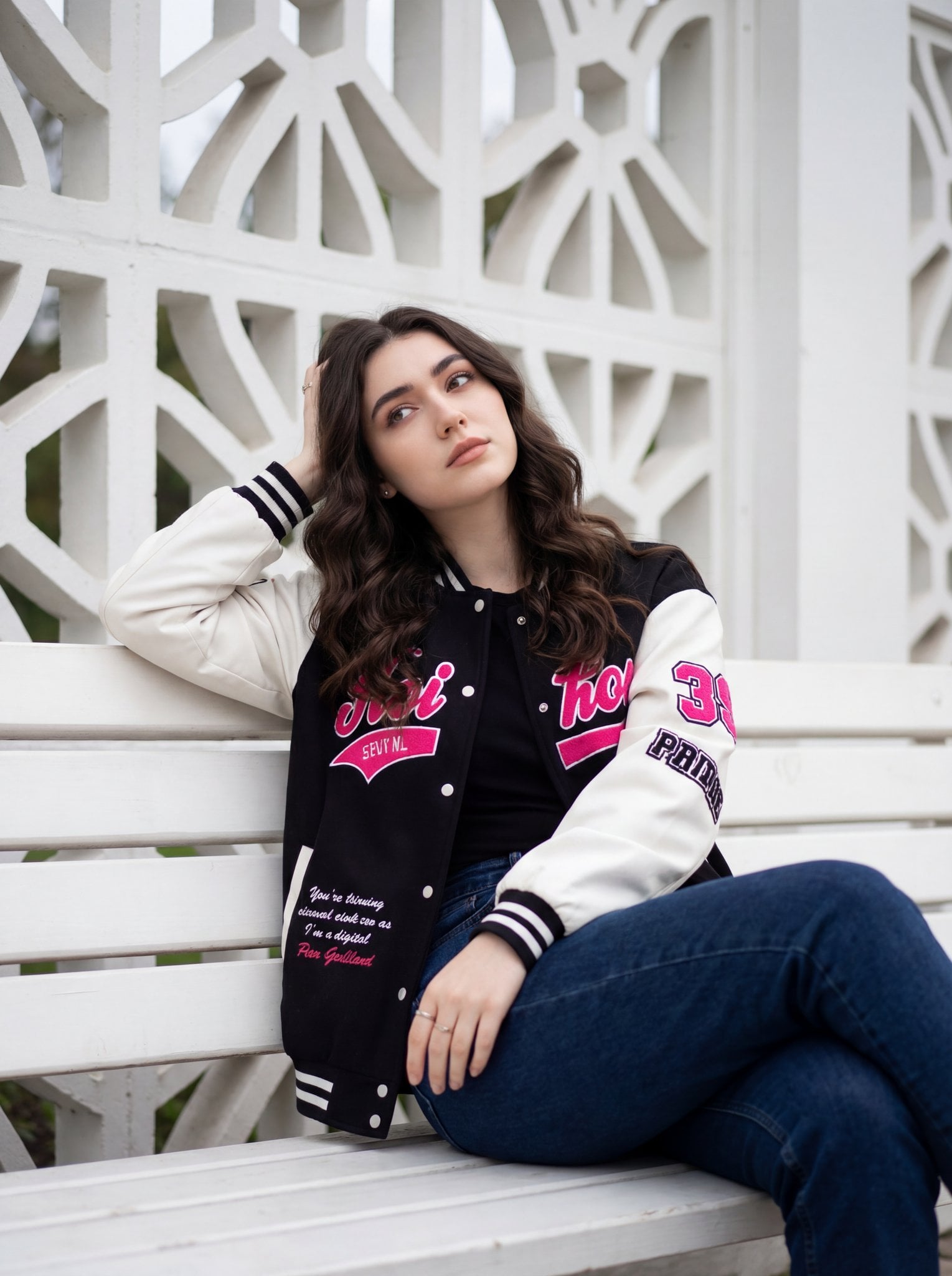 A young woman is sitting casually on a white wooden bench, positioned…