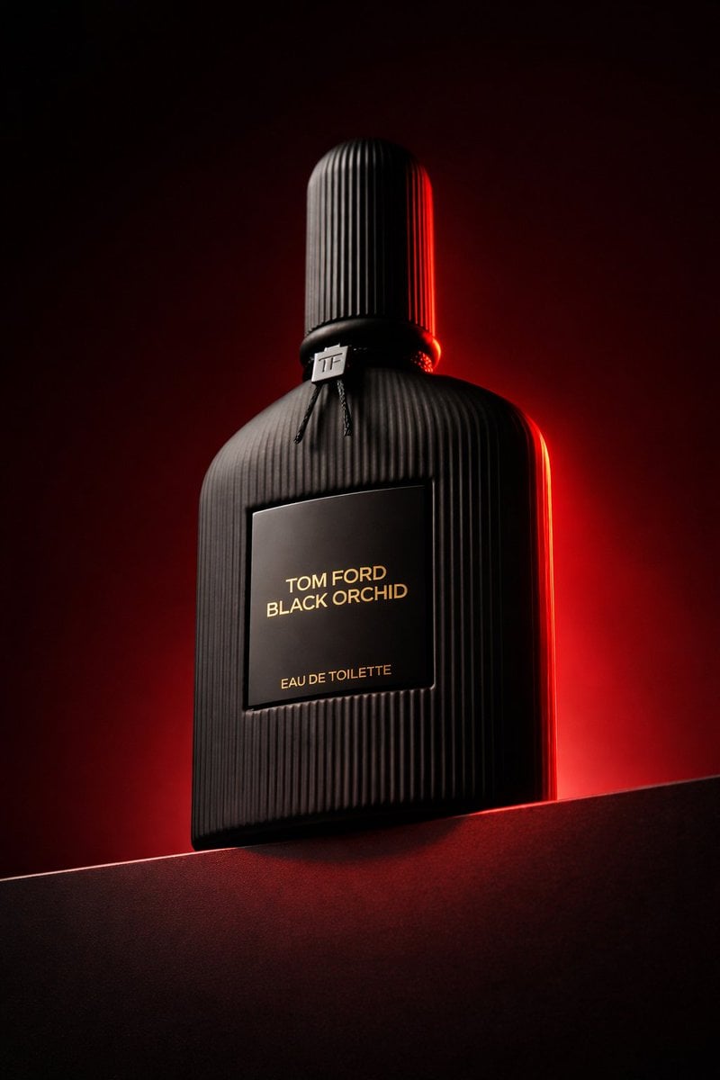 Low angle luxury product photography of a black ribbed glass perfume bottle placed on a dark horizontal podiu…