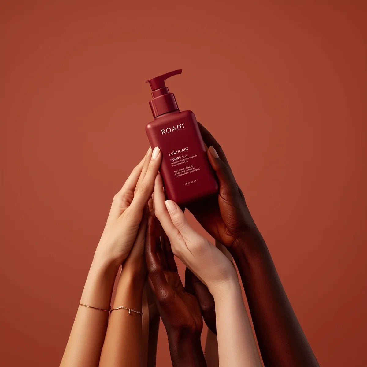 Minimalist product photography of a matte red pump bottle labeled ‘ROAM lubricant’, held by multiple diverse…