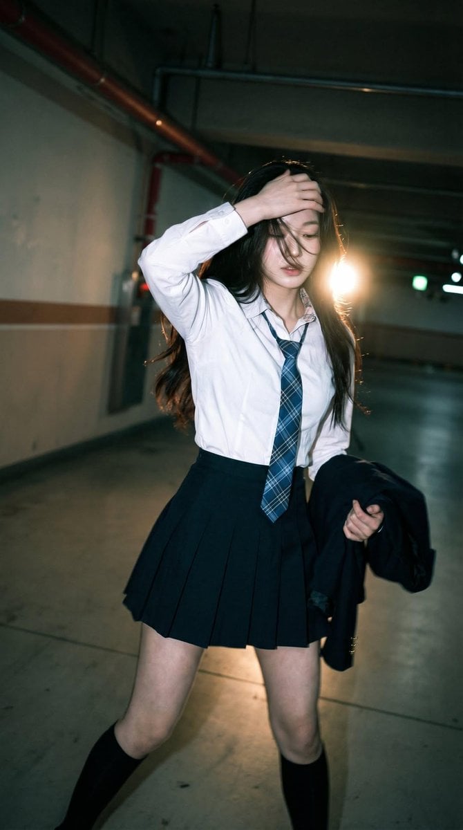 Candid portrait of a young woman in a dim parking garage, wearing a w…