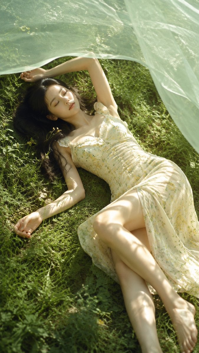 A realistic outdoor natural-light portrait of an adult young woman lying on a summer grass field, fair natura…
